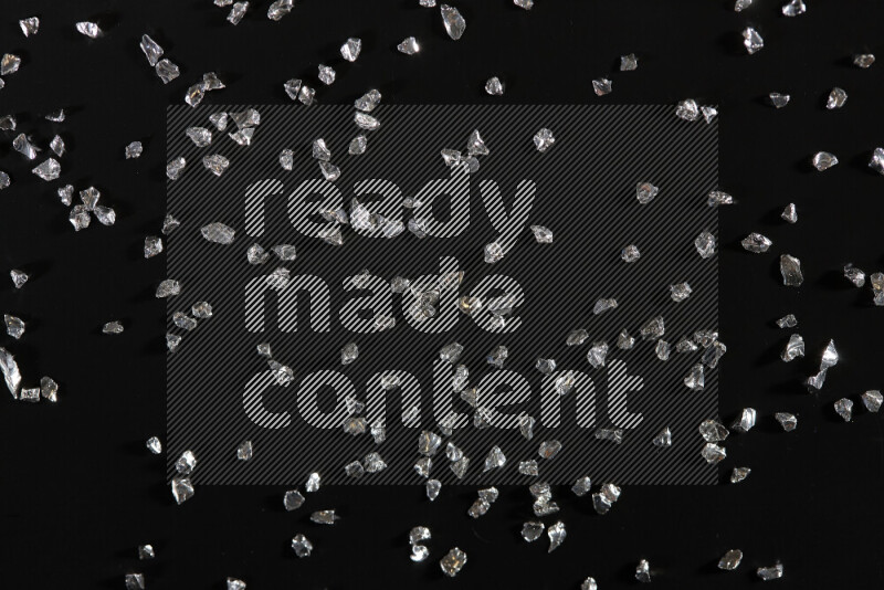 Silver shimmering fragments of glass scattered on a black background