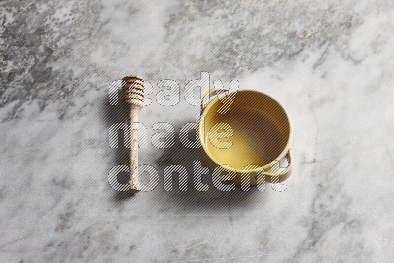 Multicolored pottery bowl with wooden honey dipper on the side on grey marble background