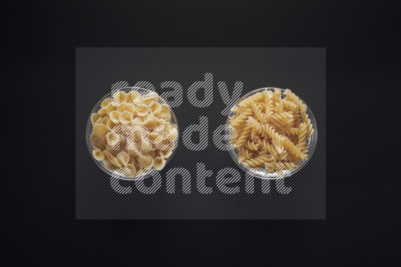 Different pasta types in glass bowls on black background