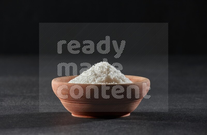 A wooden bowl full of desiccated coconut on a black background in different angles