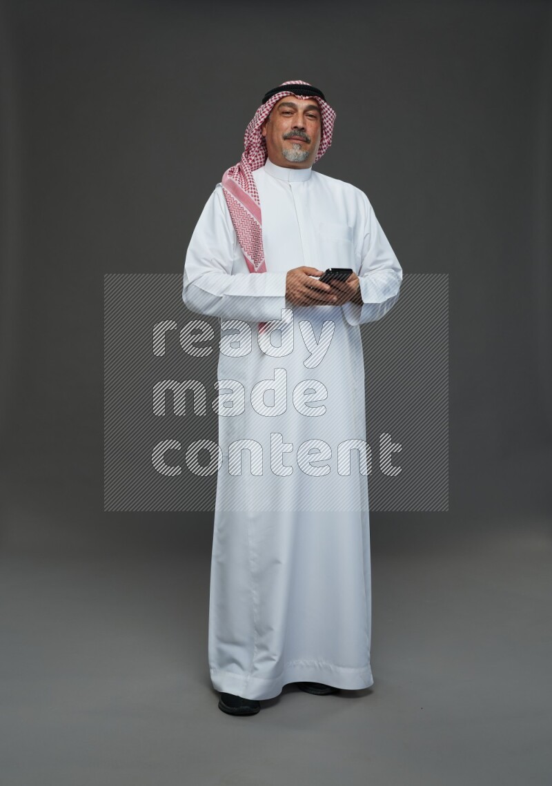 Saudi man with shomag Standing texting on phone on gray background