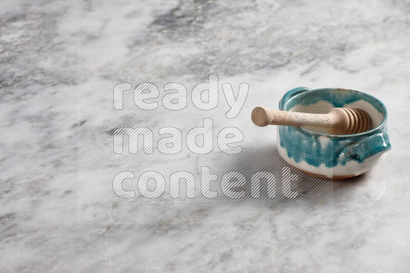 Multicolored pottery bowl with wooden honey dipper in it on grey marble background
