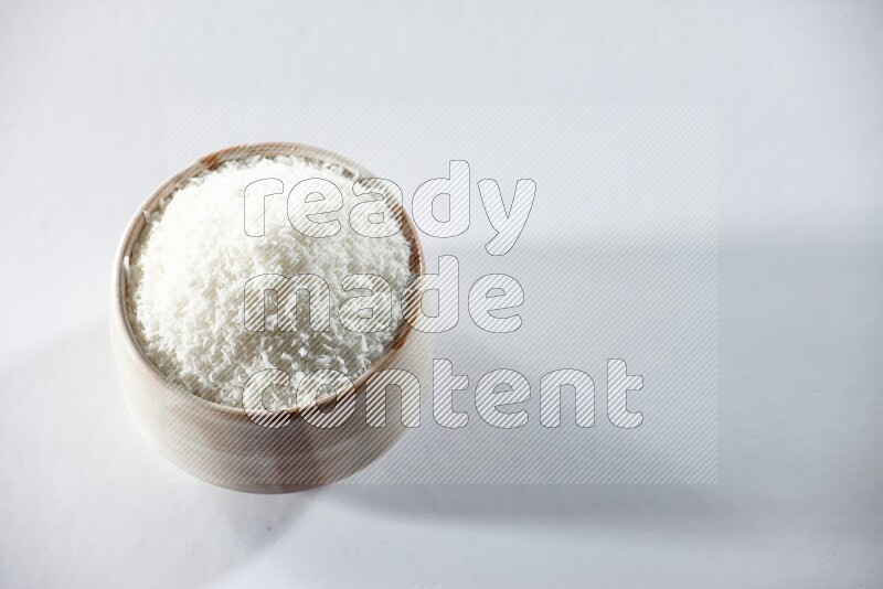A beige ceramic bowl full of desiccated coconut on a white background in different angles