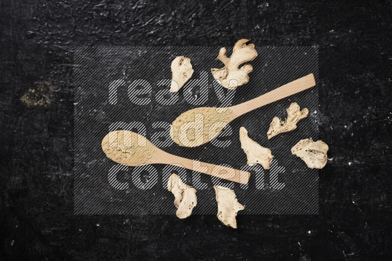 Two wooden spoons full of ground ginger powder on black background