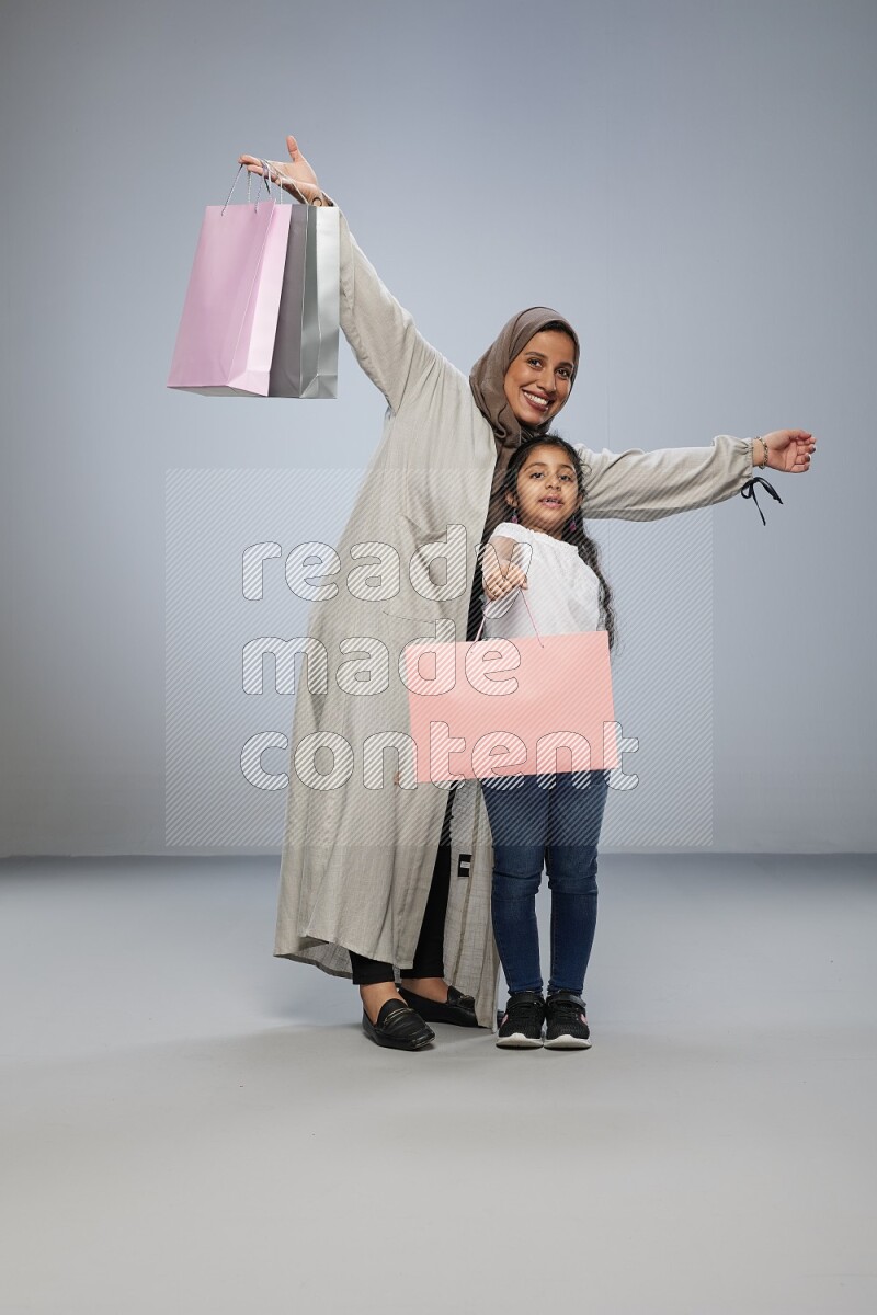 Mom and daughter holding shopping bags on gray background