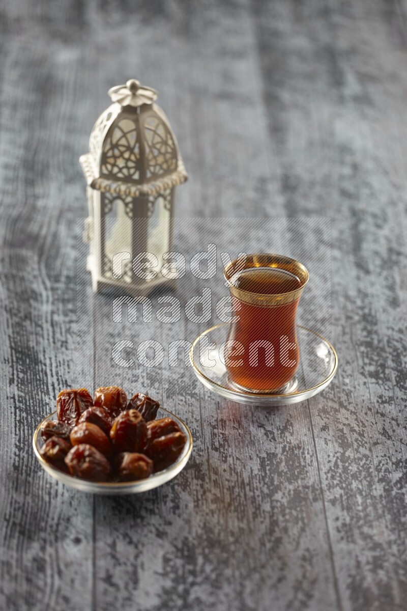 A white lantern with different drinks, dates, nuts, prayer beads and quran on grey wooden background