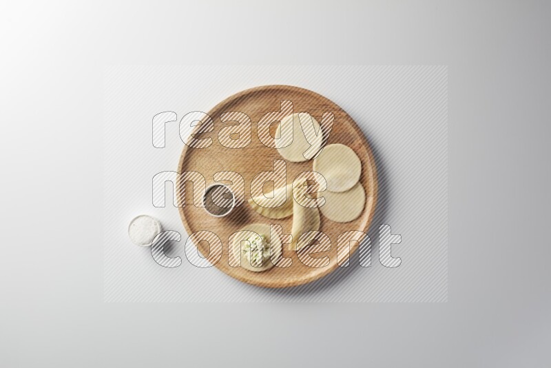 two closed sambosas and one open sambosa filled with cheese while salt, and black pepper aside in a wooden dish on a white background