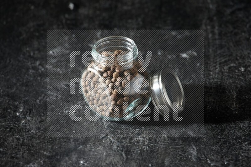 A glass spice jar full of allspice whole balls on a textured black flooring