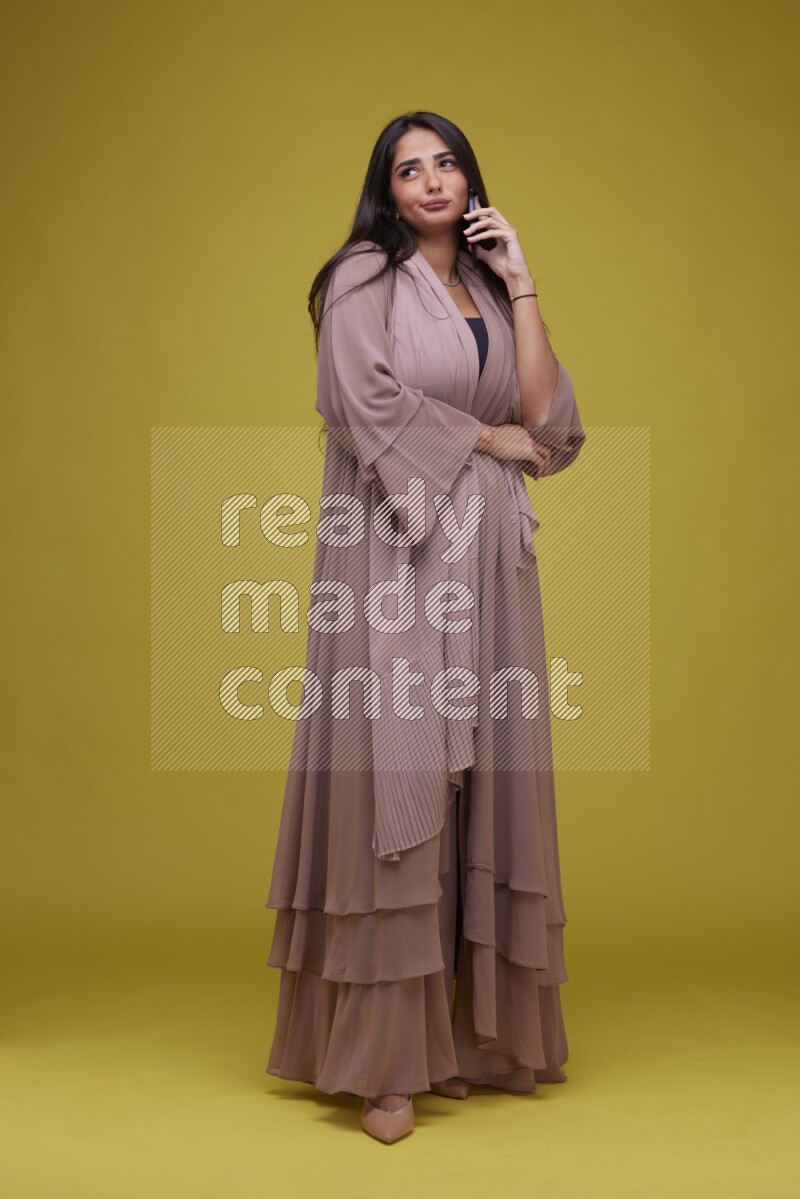 A woman Calling on a Yellow Background wearing Brown Abaya