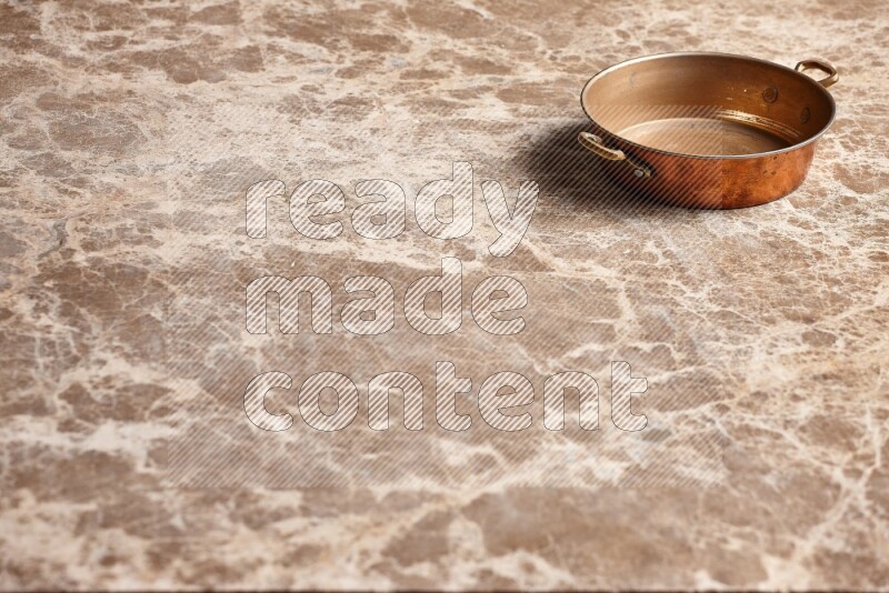 A small copper pan on beige marble background