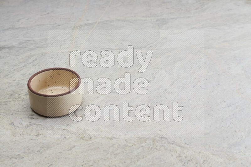 A small beige pottery bowl on grey marble background