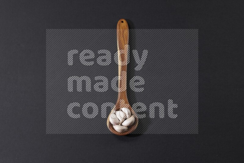 A wooden ladle full of garlic cloves on a black flooring