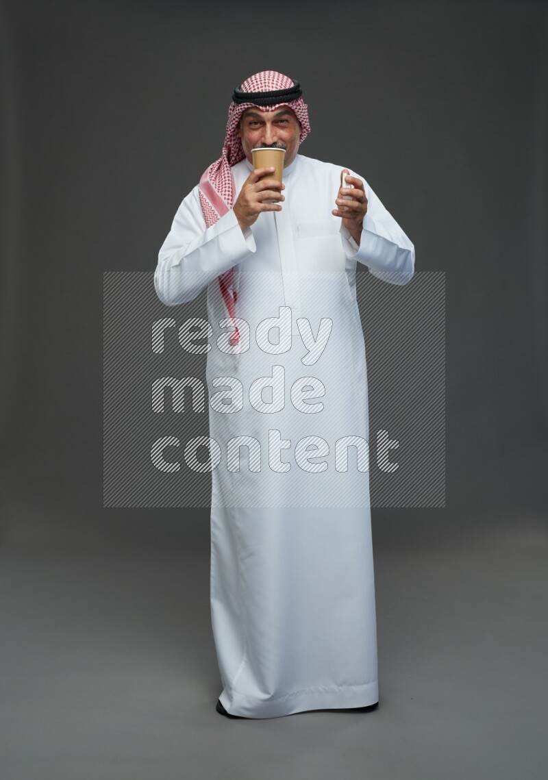 Saudi man with shomag Standing holding paper cup on gray background