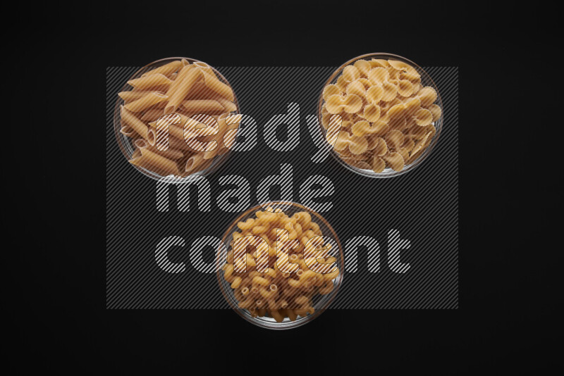 Different pasta types in glass bowls on black background