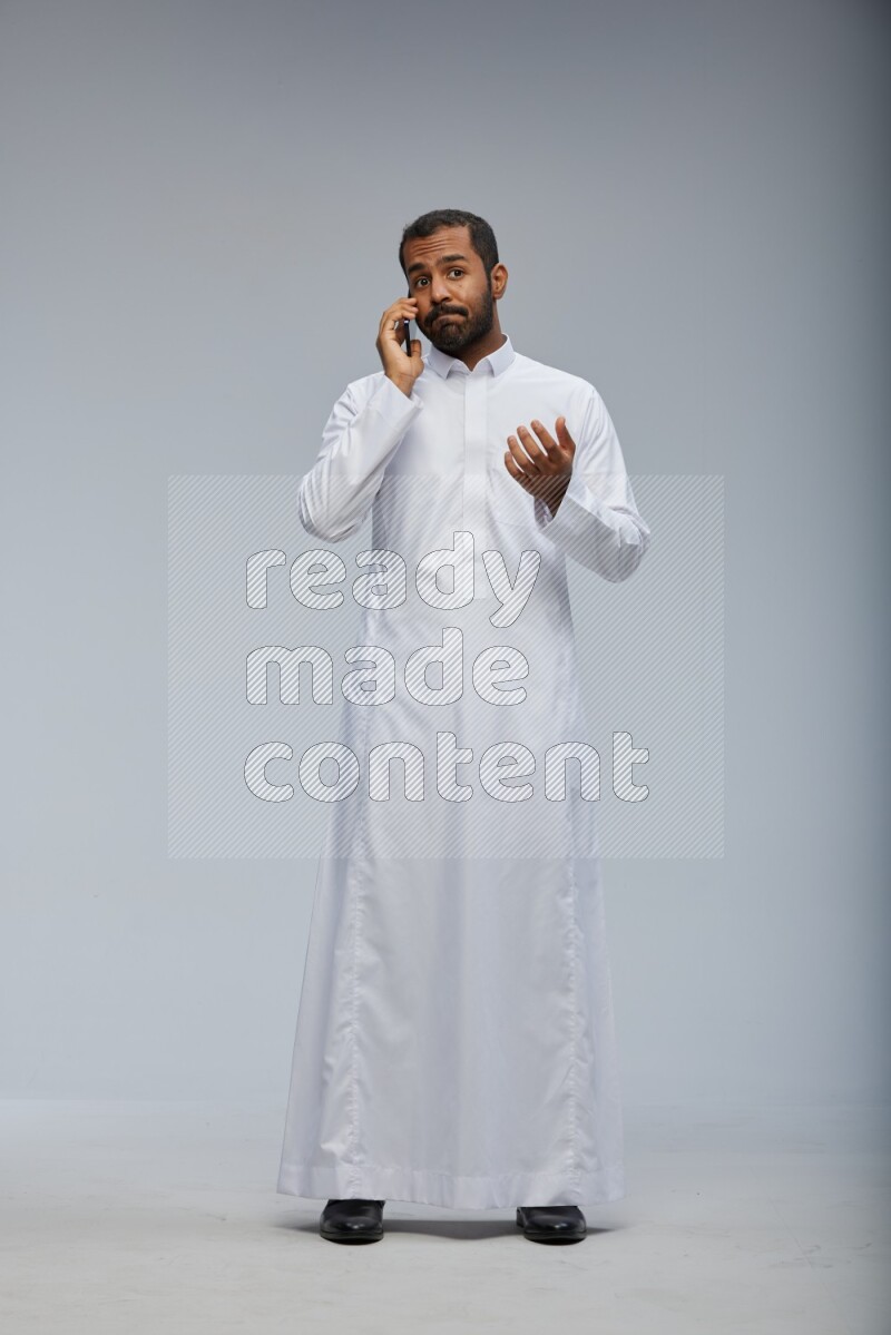 Saudi man wearing Thob standing talking on phone on Gray background