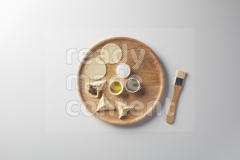 two closed sambosas and one open sambosa filled with meat while salt, black pepper and oil with oil brush aside in a wooden dish on a white background