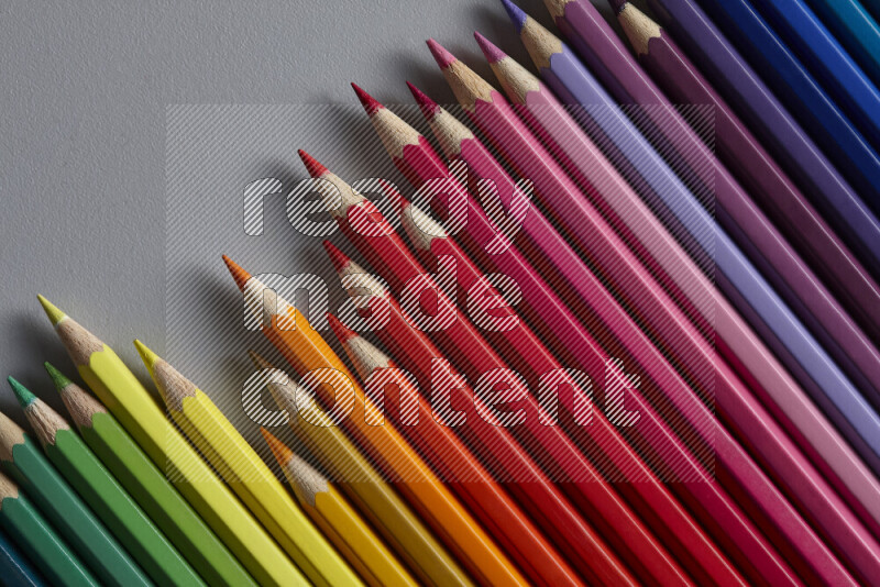 A collection of colored pencils arranged showcasing a gradient of different hues on grey background