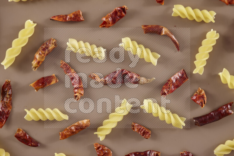Raw pasta with different ingredients such as cherry tomatoes, garlic, onions, red chilis, black pepper, white pepper, bay laurel leaves, rosemary and cardamom on beige background