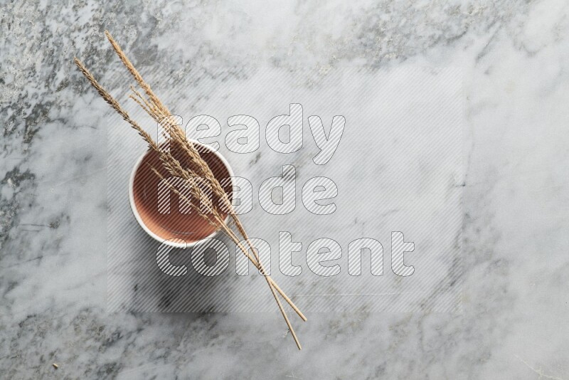 Wheat stalks on brown pottery bowl on grey marble background