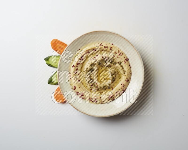 Hummus in a pottry plate garnished with zaatr & sumak on a white background