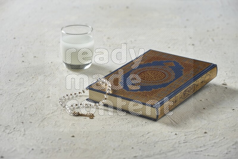 Quran with dates, prayer beads and different drinks all placed on textured white background