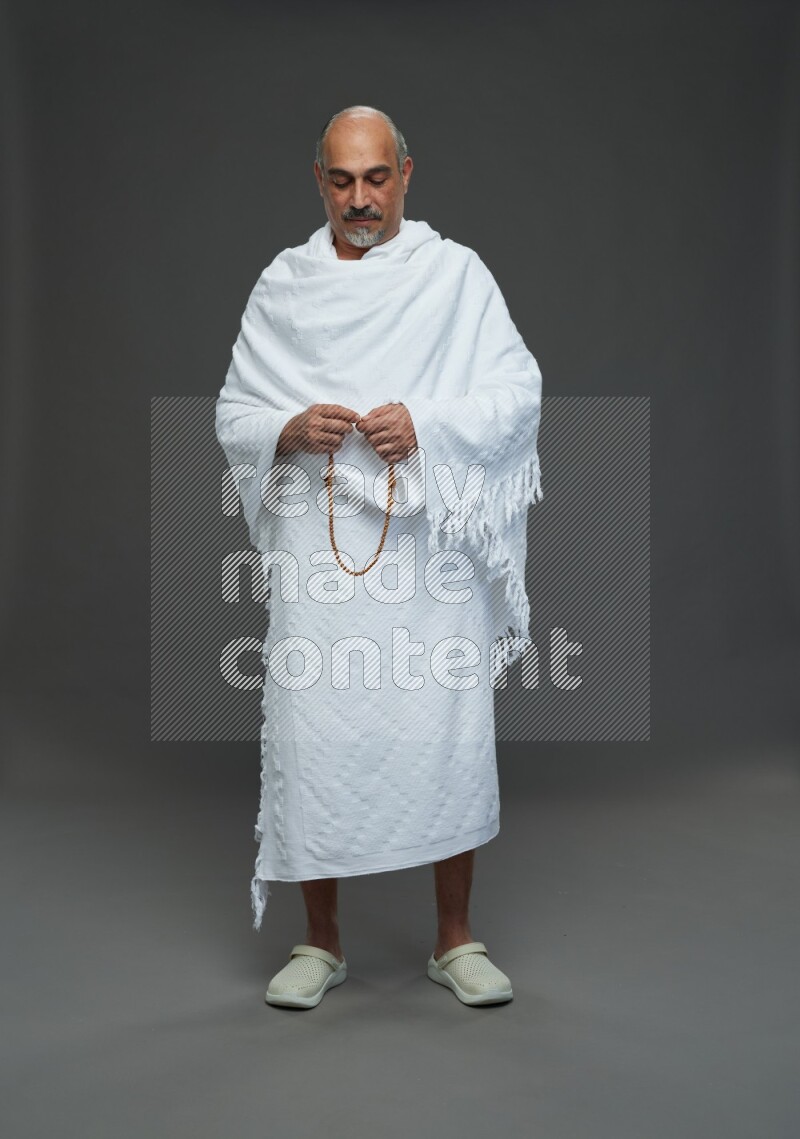 A man wearing Ehram Standing holding rosary on gray background