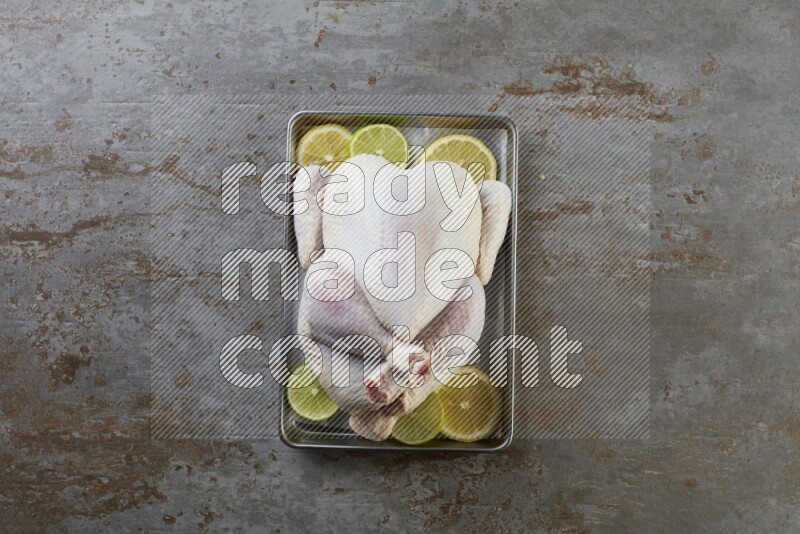 whole Raw chicken on a small oven trey direct on a rustic grey background