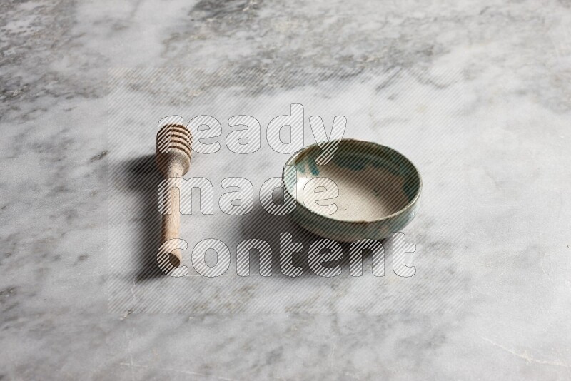 Multicolored pottery bowl with wooden honey dipper on the side on grey marble background