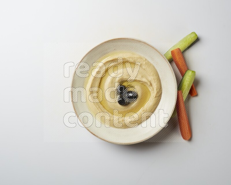 Hummus in a pottry plate garnished with black olives on a white background