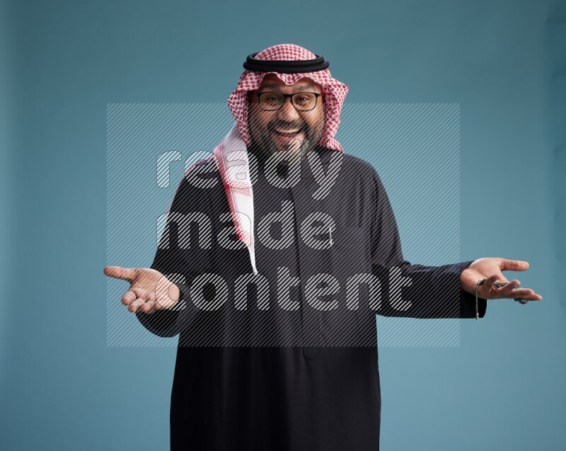 Saudi Man with shimag Standing Interacting with the camera on blue background