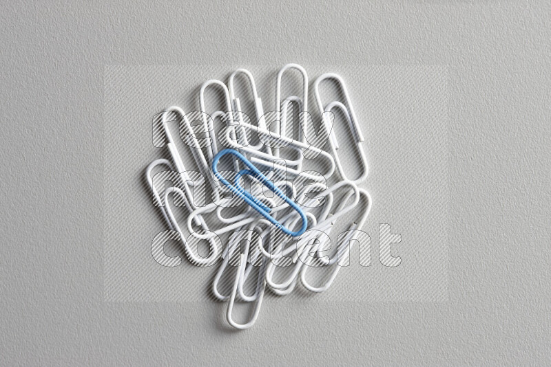 A bunch of white paper clips with a different colored paper clip in the center on grey background