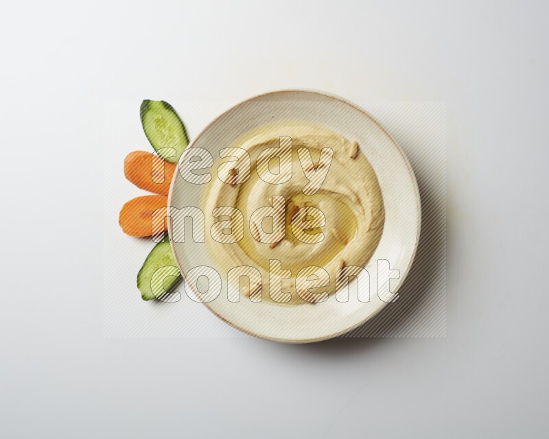 Hummus in a pottry plate garnished with pine nuts on a white background