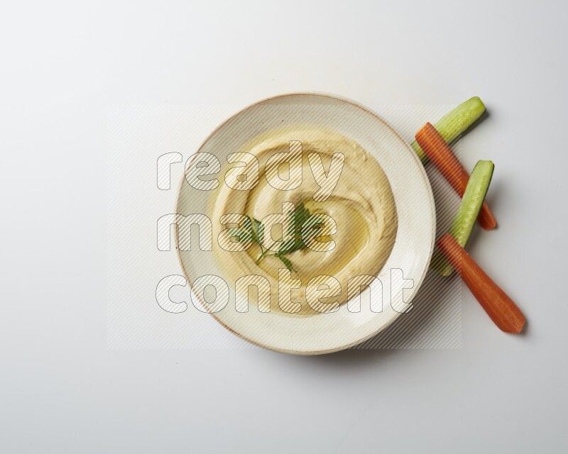 Hummus in a pottry plate garnished with parsley on a white back ground