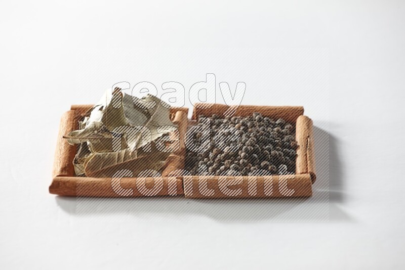 مربعان من أعواد القرفة ممتلئان بحبوب الفلفل الأسود وأوراق الغار علي خلفية بيضاء