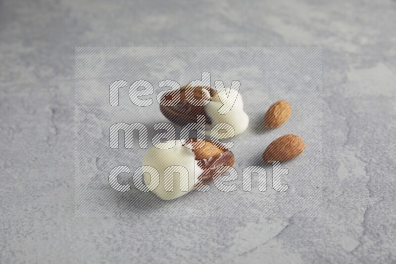 two almonds stuffed dates covered with white chololate with unroasted almonds on a light grey background