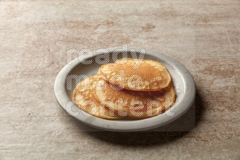 Three stacked plain pancakes in a grey plate on beige background