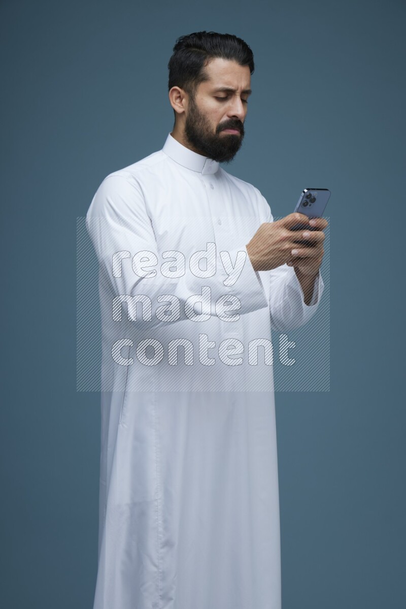 A man Texting in a blue background wearing Saudi Thob
