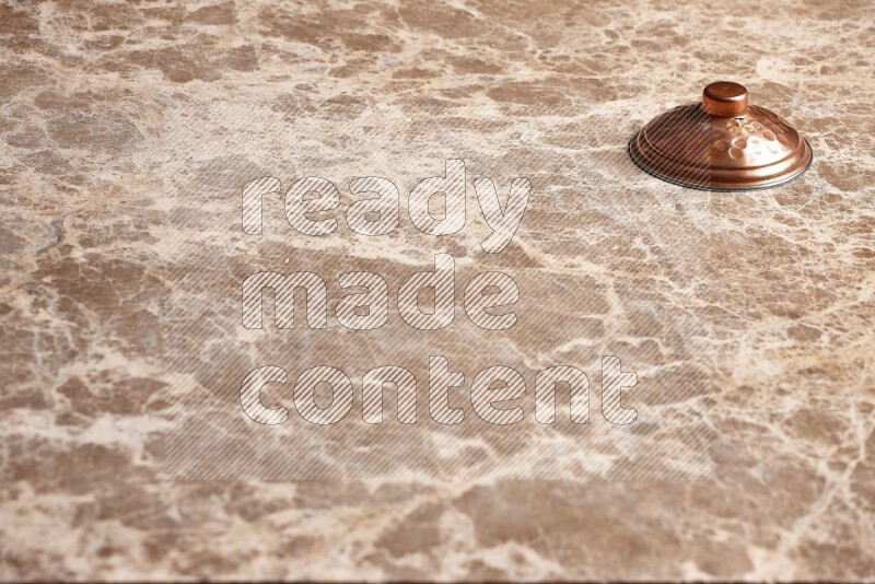 A small copper pot lid on beige marble background
