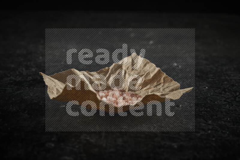 A crumpled piece of paper full of pink himalayan salt on black background