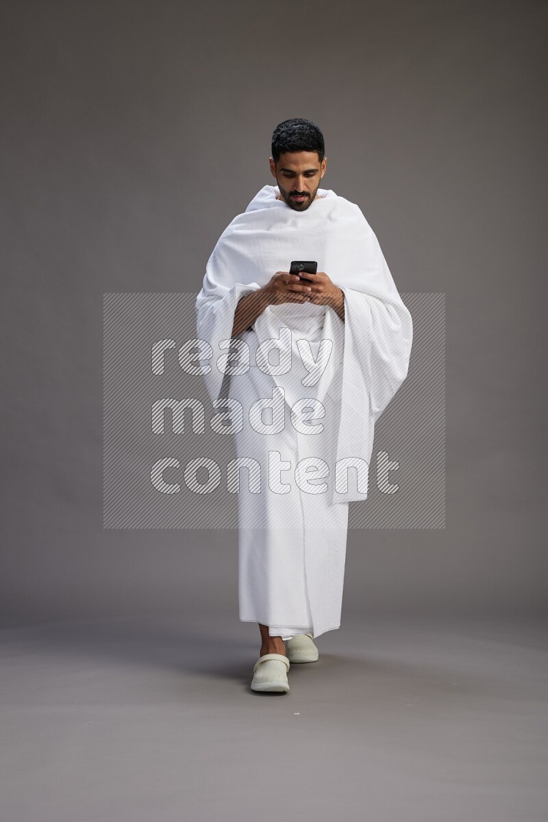 A man wearing Ehram Standing texting on phone on gray background
