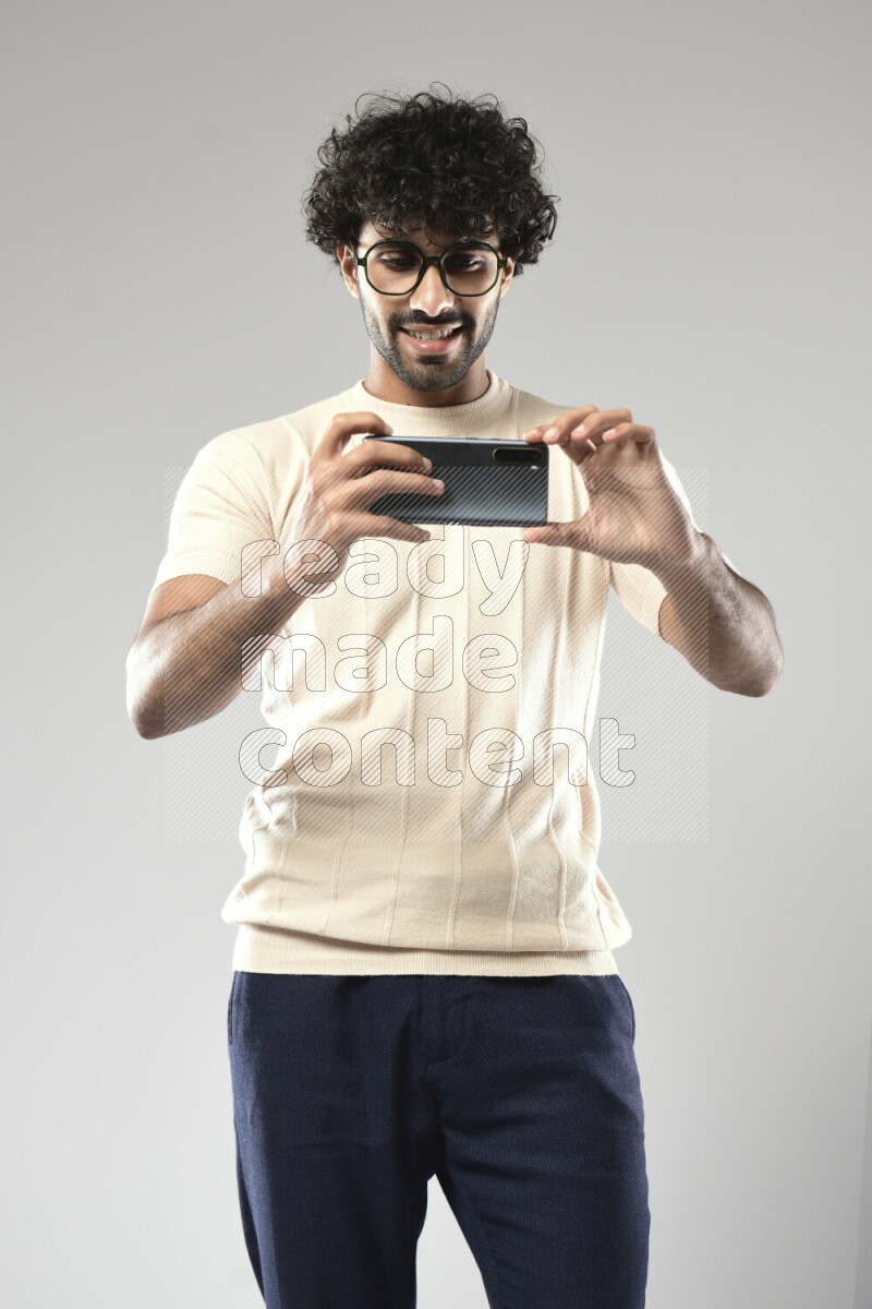 A man wearing casual standing and shooting with his phone on white background