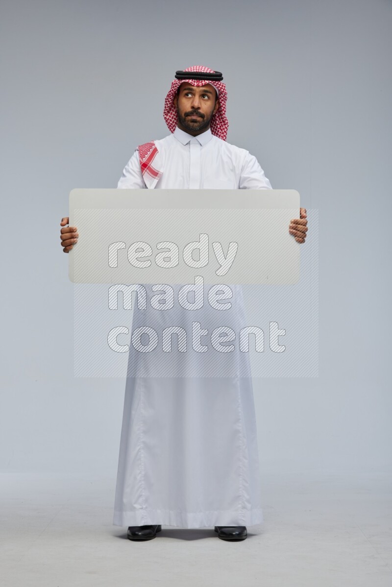 Saudi man Wearing Thob and shomag standing holding board on Gray background