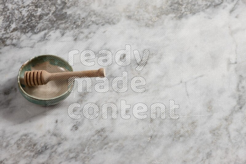 Multicolored pottery bowl with wooden honey dipper in it on grey marble background