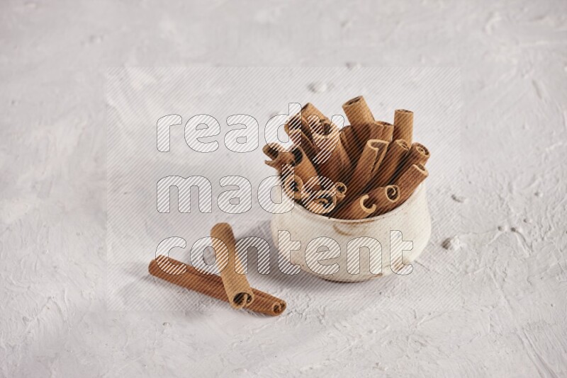 Cinnamon sticks in a beige bowl and more sticks beside it on white background