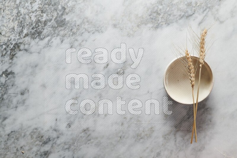 Wheat stalks on beige pottery bowl on grey marble background