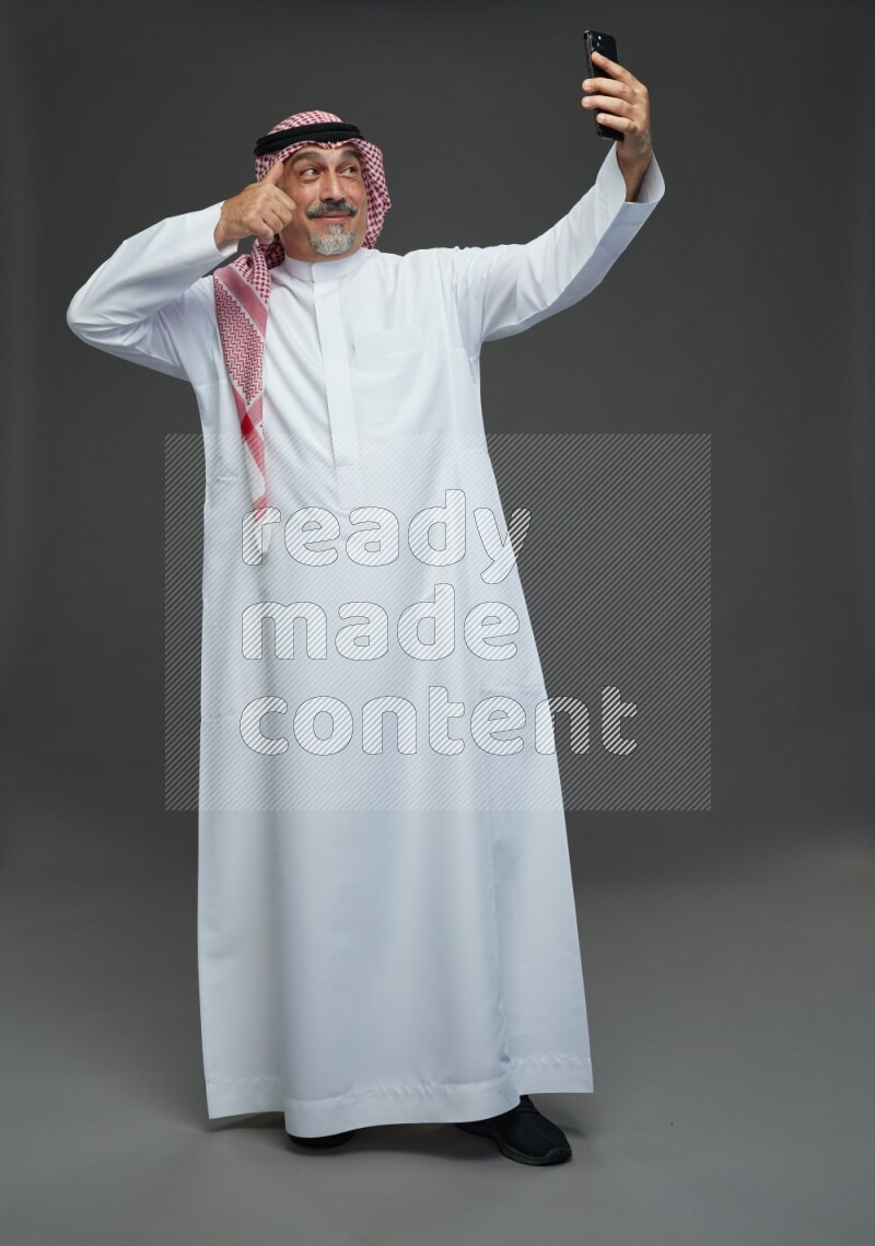 Saudi man with shomag Standing taking selfie on gray background