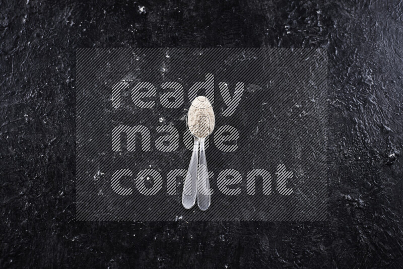 ملعقتان معدنيتان أحدهما ممتلئة ببودرة البصل علي خلفية سوداء