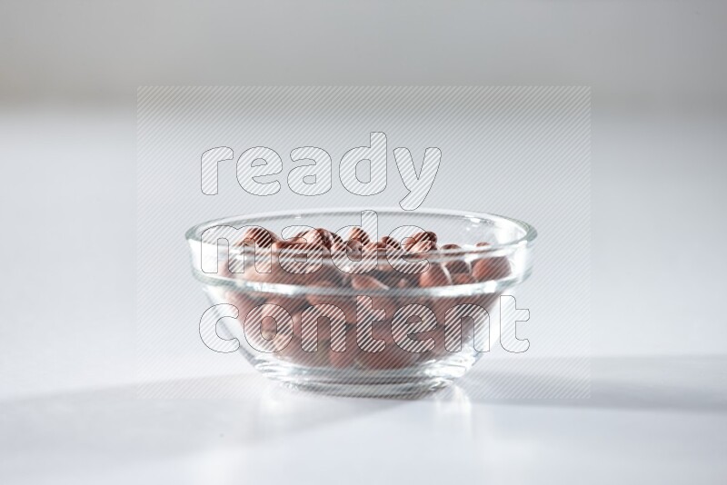A glass bowl full of red skin peanuts on a white background in different angles