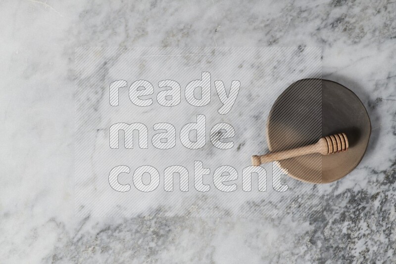 Multicolored pottery plate with wooden honey dipper in it on grey marble background
