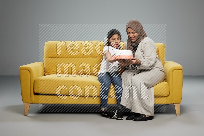A girl sitting giving a cake to her mother on gray background